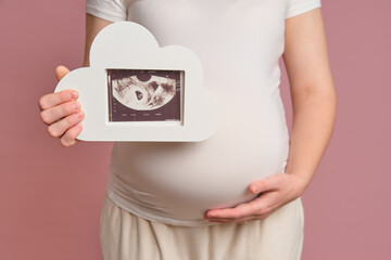 Pregnant woman holding ultrasound shot, studio pink background. Concept of pregnancy and medical...