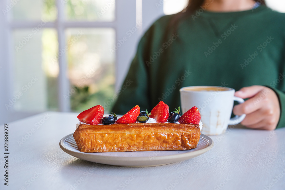 Wall mural closeup image of a woman drinking coffee with a plate of mix berry log croissant on the table