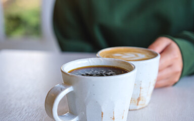 Closeup image of a woman holding and drinking coffee with friend in cafe