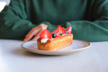Closeup image of a woman with a plate of mix berry log croissant on the table