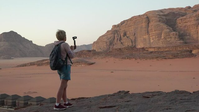 Travel and adventure. Woman tourist on sunset excursion taking pictures of landscapes in the desert. Desert sunrise tour on Wadi rum desert outdoors. Young woman hiker enjoying nature desert view.