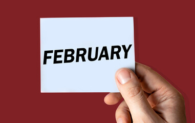 February month displayed on hand holding paper isolated on color background.