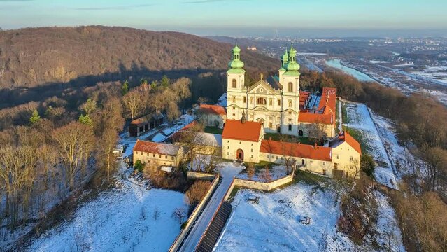 Camaldolese monastery and baroque church in the wood on the hill in Bielany, Krakow, Poland , Aerial 4K video in sunset light in winter. Far view of Vistula River and Cracow city in the background