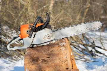 Petrol or electric battery powered chainsaw. Chainsaw on wooden stump or firewood. Firewood...