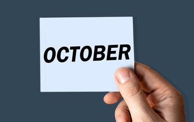 October month displayed on hand holding paper isolated on color background.