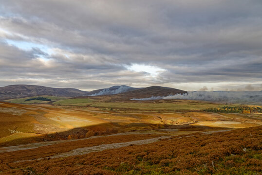 Golden sunlight on the fields and valley sides at Glen Esk during October, with Heather Burning in several places seen in the distance.