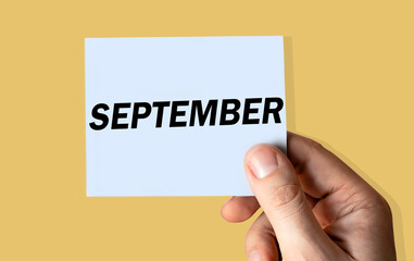September month displayed on hand holding paper isolated on color background.