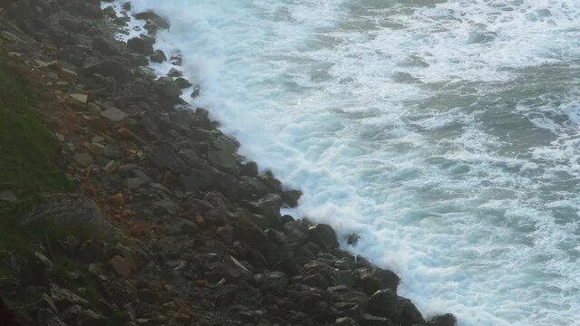 Olas rompiendo contra las rocas en un dia con sol, nubes y bruma