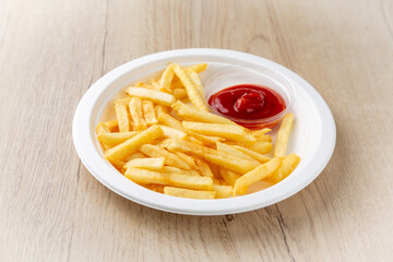 French fries with ketchup on a plate. On a light wooden background.