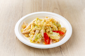 Caesar salad with chicken on a plate. On a light wooden background.