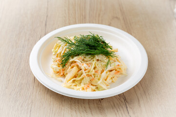 Cabbage salad with carrots on a plate. On a light wooden background.
