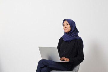 Portrait of excited Asian hijab woman in casual shirt sitting on chair, working on laptop. An employee or student doing her task and job . Businesswoman concept. Isolated image on white background