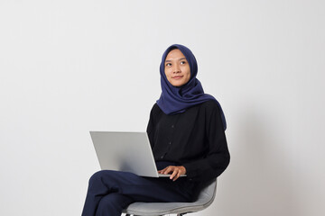 Portrait of excited Asian hijab woman in casual shirt sitting on chair, working on laptop. An employee or student doing her task and job . Businesswoman concept. Isolated image on white background