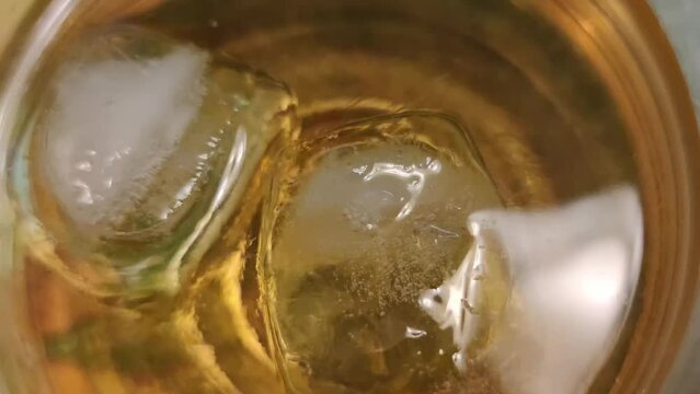 Whiskey with ice. A strong amber-colored alcoholic drink is poured into a round transparent glass goblet. Two cubes of transparent ice float in the liquid and gradually melt.