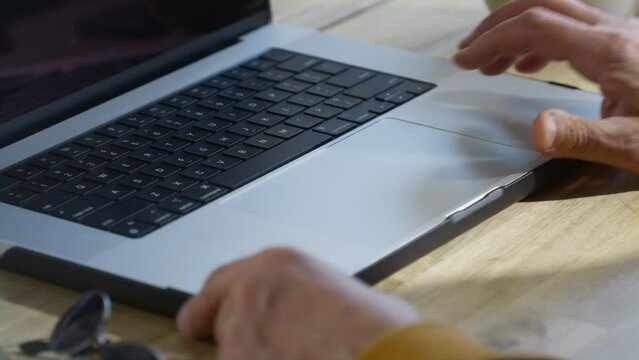 An old man opens a laptop in a restaurant. Remote work of a freelancer in a coworking. Grandpa is an IT technician or programmer. Fashionable Senior male hipster in a cafe. Modern and stylish look.
