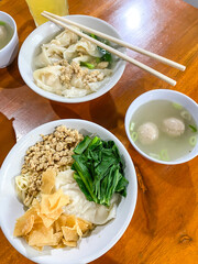 Eating chinese noodle soup topped with dumplings, chicken or beef meat, meatballs, vegetables served in ceramic bowls on a wooden table.