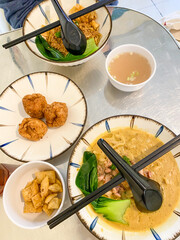 Eating chinese noodle soup topped with dumplings, chicken or beef meat, meatballs, vegetables served in ceramic bowls on a wooden table.