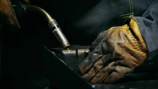 Close-up of a blacksmith welder working with metal using a welding machine, bright sparks and flashes in slow motion