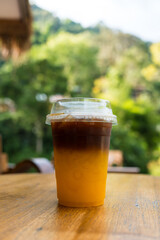 A cold brew espresso with fresh orange juice in takeaway cup, it showing the texture of two layer and refreshing look of the drink on wood table. Refreshing summer drink.