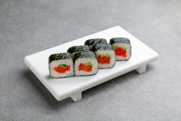 Japanese Sushi roll with salmon and cucumber in nori seaweed on a white stand, gray background