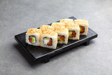 Japanese Sushi roll fried in sesame with salmon and cucumber on a black stand, gray background