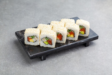 Japanese Sushi roll in sesame with avocado and salmon on a black stand, gray background