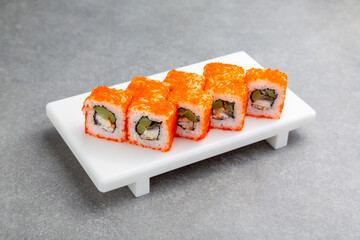 Japanese California Sushi roll with eel and cucumber on a white stand, gray background