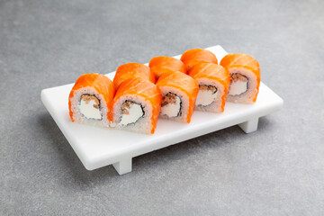 Japanese Sushi roll Philadelphia with teriyaki salmon on a white stand, gray background