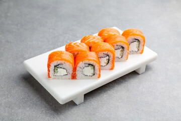 Philadelphia sushi roll with salmon and cucumber on a white stand, gray background