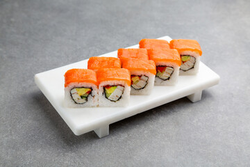 Japanese Sushi roll with salmon, avocado and crab meat on a white stand, gray background