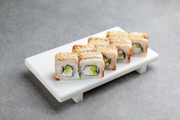 Japanese Sushi roll with eel, sesame and avocado on a white stand, gray background