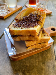 Pile of Roasted toast with chocolate sprinkles next to small fork on wooden tray on wooden table. Concept for breakfast menu.