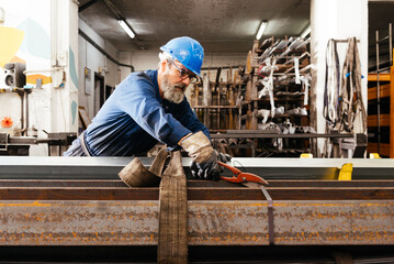 Male worker using cutting tool with metal beams bundles in workshop