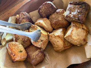 Someone picking tahu bacem with tongs on paper plate, traditional authentic typical snack from Java.