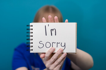 Dziewczynka trzyma kartkę z napisem po angielsku przepraszam