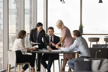 Busy diverse managers giving paper documents to boss for signing. Business team doing paperwork, analyzing sales reports together, working together, talking at meeting table