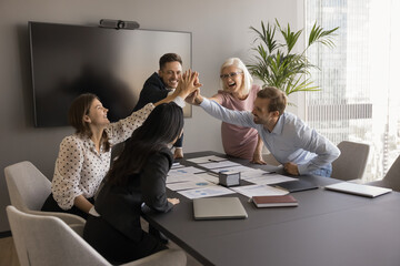 Diverse team of cheerful business colleagues giving group high five over successful sales reports,...