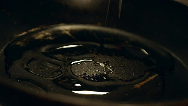 A home cook pours vegetable oil into a non-stick pan. The oil spreads smoothly over the black hot surface.