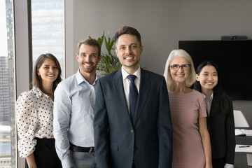 Happy attractive professional colleagues of different ages and races standing behind young male...