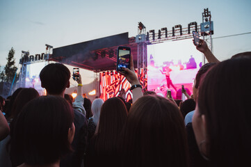 crowd of people at the stage at a live music concert are shooting videos on smartphones in their...