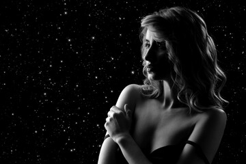 Fashionable photo of elegant girl with nice wavy hairstyle, bare shoulders. Serious sad woman on stars background with copy space, monochrome