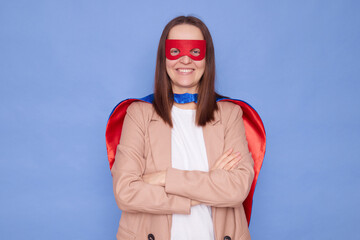Confident delighted brown haired woman wearing superhero costume posing isolated over blue background looking at camera with toothy standing with crossed arms