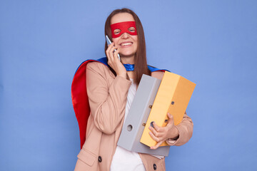 Satisfied happy cheerful brown haired woman wearing superhero costume holding paper folders posing...