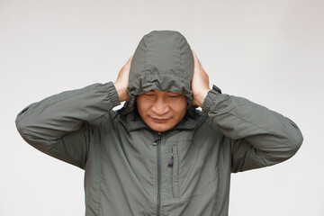 Asian man wears hoodie, uses his hands to cover ears. Concept, don't want to listen or hear...