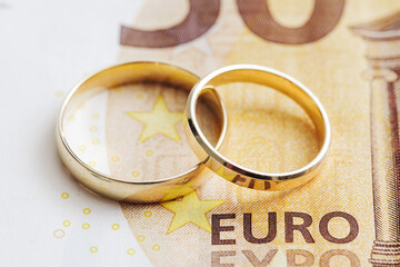Wedding rings on money. Cost of wedding. Price of getting married background. Golden jewelry on banknote. Cash for getting divorced. Expensive marriage. Fifty euro note.
