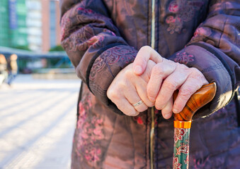 hands of an unrecognizable elderly woman holding a cane on the street