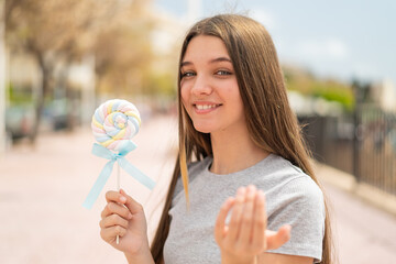 Teenager girl holding a lollipop inviting to come with hand. Happy that you came