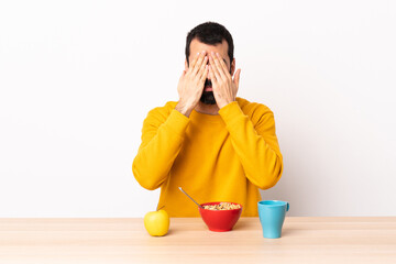 Caucasian man having breakfast in a table covering eyes by hands.
