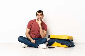 Caucasian handsome man with a suitcase full of clothes sitting on the floor at indoors showing a...