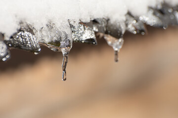 The icicles are melting from eaves of roof in end of winter. Thaw and ice melting. Drops of water...